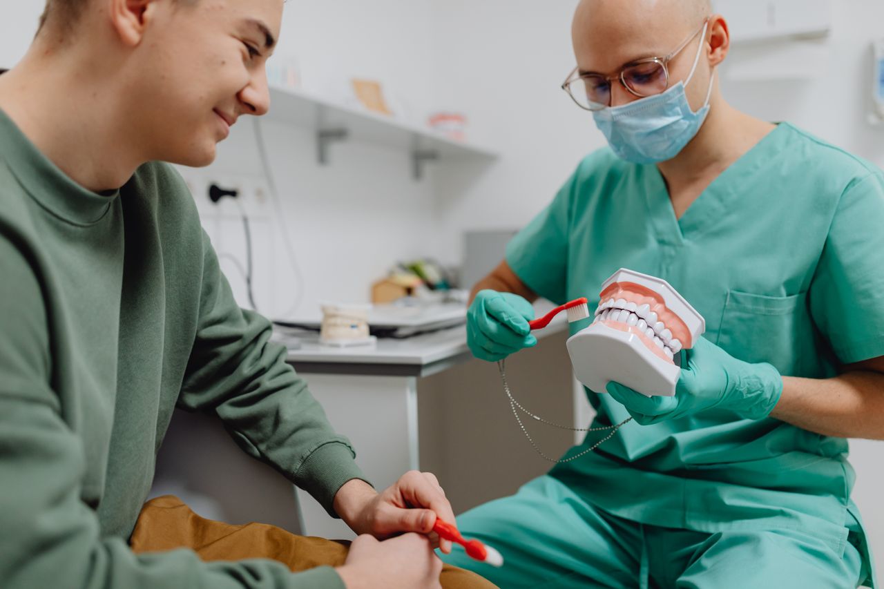 our-story A dentist demonstrates proper dental hygiene to a patient using a model.