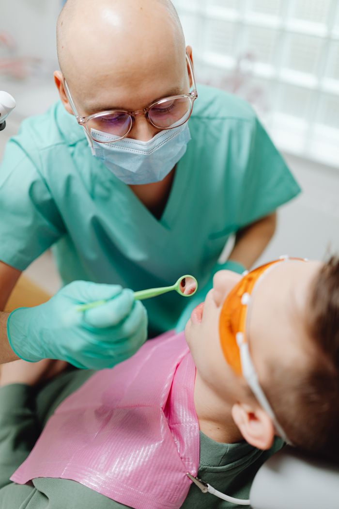 Dentist in green gown carefully examines a child's teeth in a clinic setting.